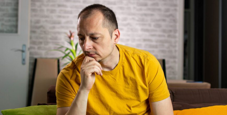 man-sitting-on-a-couch-resting-his-chin-on-his-hand-and-looking-away