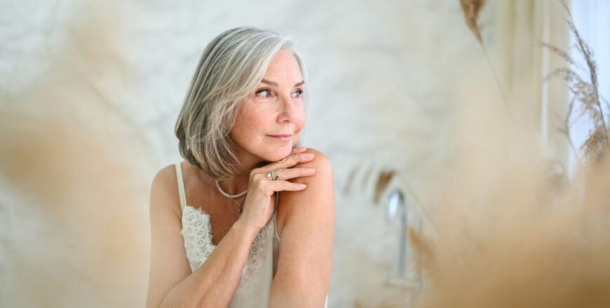 older-woman-with-gray-hair-resting-her-chin-on-her-hands-near-a-sunlit-window