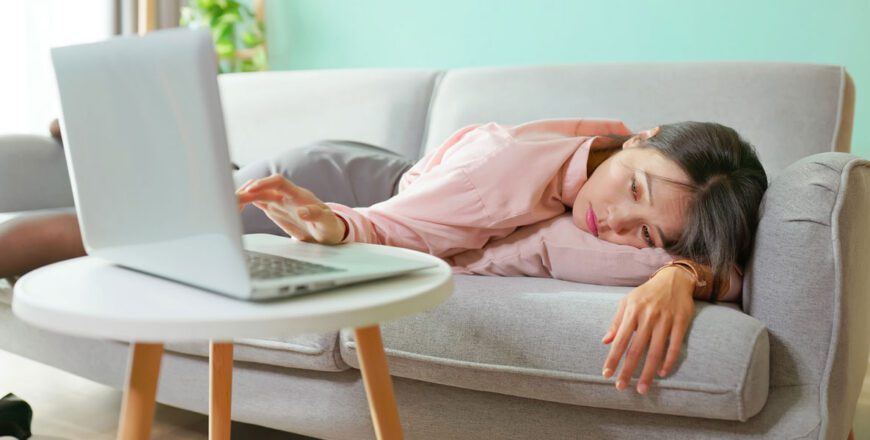 woman-lying-on-a-couch-with-her-head-down-next-to-an-open-laptop