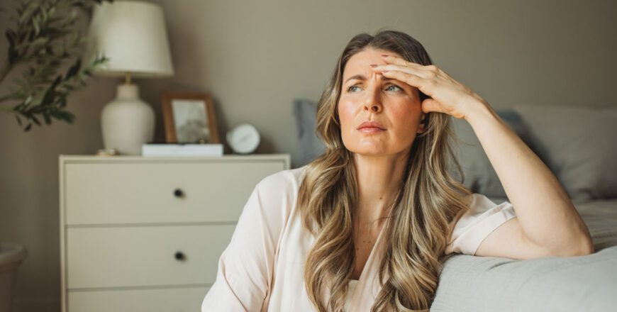 woman-sitting-on-the-edge-of-a-bed-wiping-her-forehead